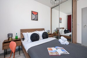 A hotel room with a bed, a nightstand, a chair, a mirror, and a magazine on the bed. - Flat near Koneser Center (Warszawa)