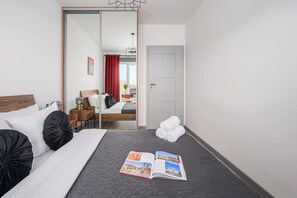 Ein Hotelzimmer mit Bett, Nachttisch, Spiegel, Tür und Blick auf eine Stadtlandschaft durch das Fenster.