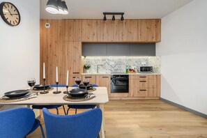 A modern kitchen with wooden cabinets, a dining area with blue chairs, and a clock on the wall. - Flat near Koneser Center (Warszawa)