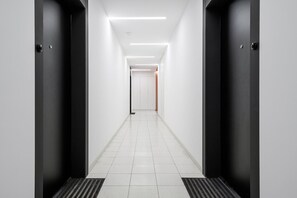 A corridor with two black doors, white walls, and a tiled floor. - Flat near Koneser Center (Warszawa)