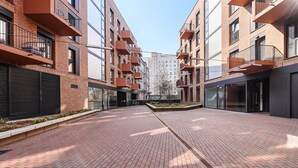 Une cour dallée de briques, des bâtiments modernes dotés de balcons et un ciel dégagé.