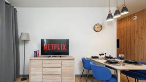 Un salon moderne avec un téléviseur affichant le logo « NETFLIX », un coin repas avec des chaises bleues et un meuble en bois.
