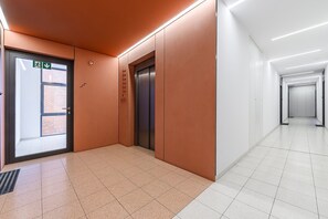 An interior corridor with a door marked for accessibility, an elevator, and a tiled floor. - Flat near Koneser Center (Warszawa)