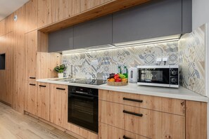 A modern kitchen with wooden cabinets, a microwave, a dishwasher, and a fruit basket on the counter. - Flat near Koneser Center (Warszawa)