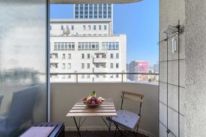 Ein Balkon mit Tisch und Stuhl, einer Obstschale und Blick auf die Stadtlandschaft.