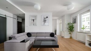 Ein modernes Wohnzimmer mit einem grauen Ecksofa, einem schwarzen Couchtisch und Holzboden. Zwei Wandleuchten und zwei gerahmte Kunstwerke sind über der Couch angebracht.