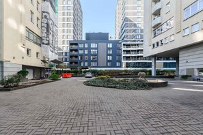 Un immeuble résidentiel moderne doté d’une cour pavée, entouré d’immeubles d’habitation de grande hauteur.