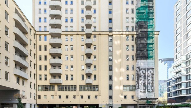 Ein mehrstöckiges Wohngebäude mit Balkonen, einem verschlossenen Eingangsbereich und einer Baustelle auf der rechten Seite.