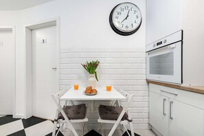 Eine moderne Küche mit weißen Schränken, einer weißen Fliesenküche, einer Wanduhr, einem weißen Tisch mit Stühlen, einer Vase mit Blumen und einem Frühstückstisch mit Croissants und Orangensaft.