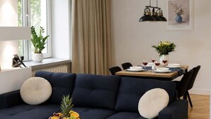 Ein modernes Wohnzimmer mit einem dunkelblauen Sofa, einem Esstisch für vier Personen und einem großen Fenster mit Vorhängen.