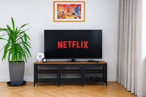 Ein Wohnzimmer mit Fernseher, der 'NETFLIX' anzeigt, einer Topfpflanze und einem gerahmten Bild an der Wand.