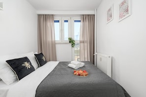 A hotel room with a bed, a radiator, a window with curtains, and a plant. - Central City Apartment with Balcony in Warsaw (Warszawa 2)