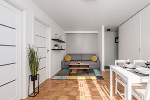 A modern living room with a sofa, coffee table, and dining area. - Central City Apartment with Balcony in Warsaw (Warszawa 2)