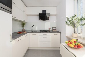 A modern kitchen with white cabinets, a gas stove, a sink, and a window with a view of the outside. - Central City Apartment with Balcony in Warsaw (Warszawa 2)