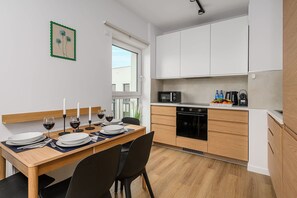 A modern kitchen with white cabinets, a dining table set for four, and a view of the outside. - Łódź City Apartment with Balcony (Łódź)