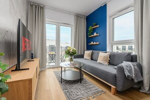A modern living room with a grey sofa, a round coffee table, a flat-screen TV, and a balcony with a city view. - House in France near Plage du Bourg Beach (Łódź)