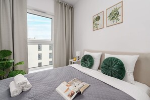 A hotel room with a large bed, a window with curtains, a bedside table with a lamp, and two framed botanical prints on the wall. - House in France near Plage du Bourg Beach (Łódź)