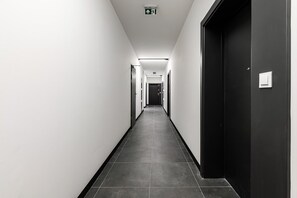 Un long couloir étroit, avec une porte noire sur la droite et une porte blanche sur la gauche.