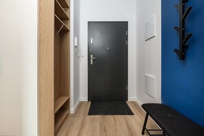 Un couloir avec une armoire en bois, une porte noire, un banc noir et un mur bleu.