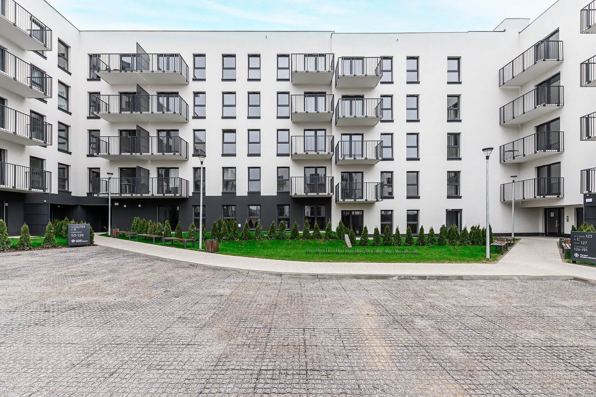 Un immeuble résidentiel à plusieurs étages, doté de balcons, d’une cour pavée et d’espaces verts.