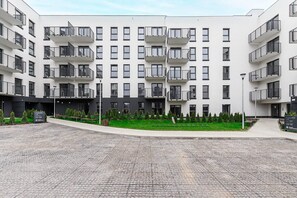 Un immeuble résidentiel à plusieurs étages, doté de balcons, d’une cour pavée et d’espaces verts.