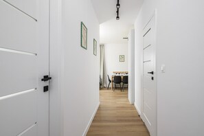 Un couloir avec des portes blanches, un coin repas avec une table et des chaises, et un luminaire au plafond.