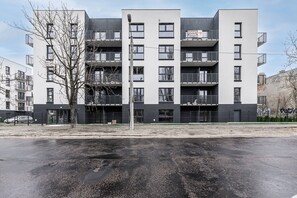 A multi-story residential building with balconies, a parking lot in front, and a tree to the left. - House in France near Plage du Bourg Beach (Łódź)