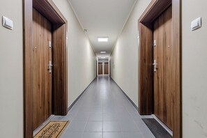 A long, narrow hallway with wooden doors on either side and a tiled floor. - Beautiful Flat with Garage (Łódź)