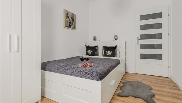 A bedroom with a bed, a wardrobe, a door with glass panels, and a picture on the wall. - Beautiful Flat with Garage (Łódź)