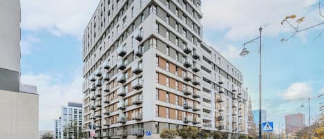 A multi-story residential building with balconies, a pedestrian crossing, and a clear sky.