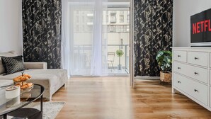 A modern living room with a sofa, a coffee table, a TV, and a balcony with curtains. - Beautiful Flat with Garage (Łódź)