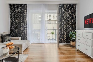 A modern living room with a sofa, a coffee table, a TV, and a balcony with curtains. - Beautiful Flat with Garage (Łódź)