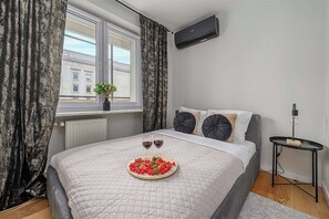 Ein Schlafzimmer mit einem Bett, einem Nachttisch, einem Fenster mit Vorhängen und einer Wand-Klimaanlage.