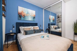 A modern bedroom with a large bed, a bedside table, a nightstand, a mirror, and a potted plant. - Family Apartment near Vistula River (Warszawa 2)