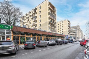 Straßenansicht mit parkenden Autos, einem Café und einem Gebäude mit Balkonen.