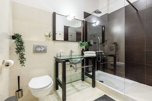 A modern bathroom with a glass sink, dark tiles, a toilet, and a shower area. - Stylish Apartment in Mariensztat for 6 (Warszawa)