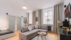 Een moderne woonkamer met een grijze hoekbank, een klein rond salontafeltje en een televisie die aan de muur is bevestigd.