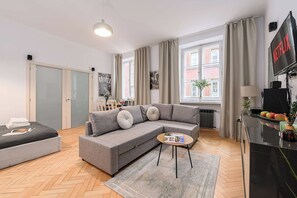 Ein modernes Wohnzimmer mit einem grauen Ecksofa, einem kleinen runden Couchtisch und einem an der Wand montierten Fernseher.