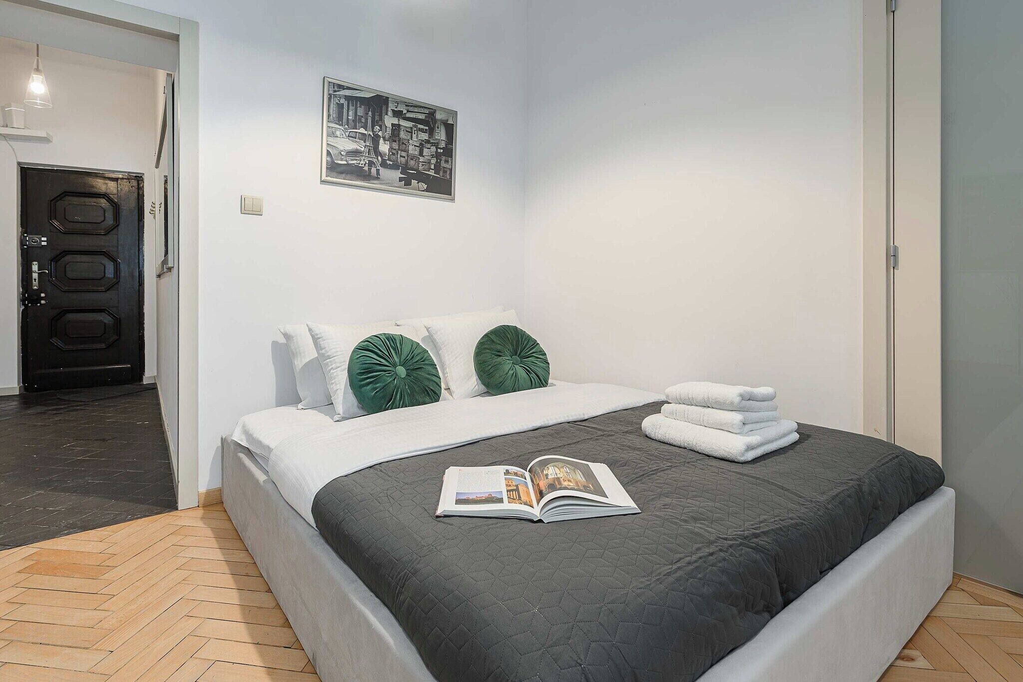 Un lit bien fait, avec une couverture sombre, deux oreillers verts et un magazine posé sur le lit.