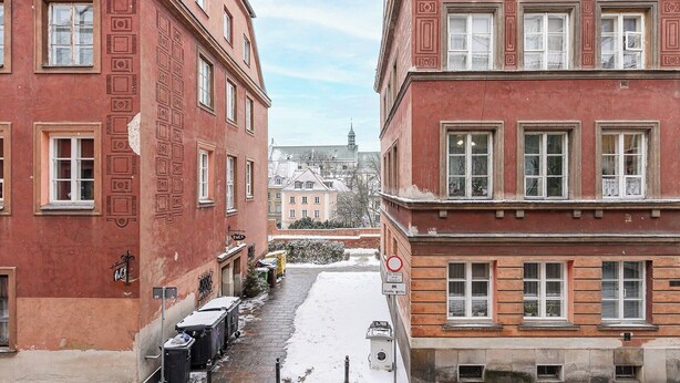 Een smalle straat met rode bakstenen gebouwen, sneeuw op de grond en een heldere lucht.