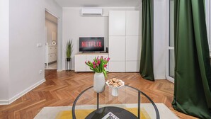 A modern living room with a flat-screen TV, a vase with flowers, a plate of cookies, and a herringbone-patterned wooden floor. - Waterfront House in Ploudalmézeau (Warszawa 2)