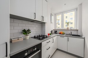 Eine moderne Küche mit weißen Schränken, einem Gasherd, einer Spüle und einem Fenster mit Blick auf Gebäude.