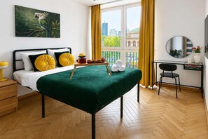Ein Hotelzimmer mit Bett, Schreibtisch, Stuhl, einem Fenster mit Vorhängen, einem Bild an der Wand und Blick auf die Stadt.