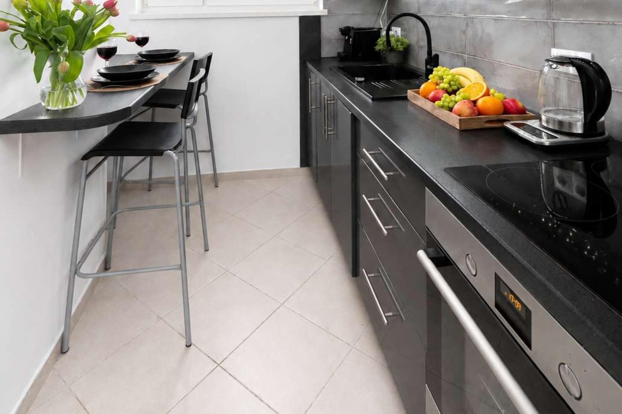 A modern kitchen with a black countertop, stainless steel appliances, and a fruit bowl.