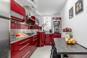 A modern kitchen with red cabinetry, stainless steel appliances, and a fruit bowl on the island. - City Apartment in Warsaw (Warszawa 2)