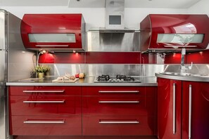 A modern kitchen with red cabinetry, stainless steel appliances, and a central island with a sink. - City Apartment in Warsaw (Warszawa 2)
