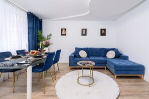 A modern living room with a blue sofa, a dining table with chairs, and a white rug. - City Apartment in Warsaw (Warszawa 2)