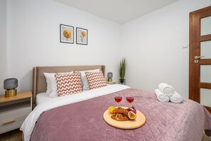 A neatly made bed with a pink quilt, two pillows, a bedside table with a lamp, and a wall-mounted picture. - City Apartment in Warsaw (Warszawa 2)