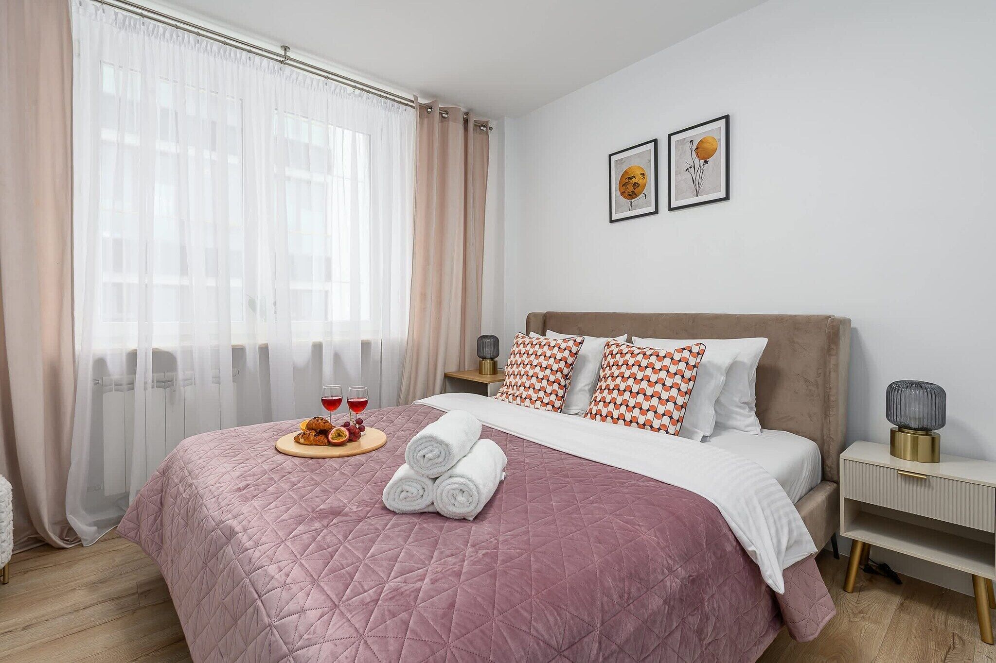 Ein Hotelzimmer mit Bett, Nachttisch, Lampe und einem Fenster mit durchscheinenden Vorhängen.