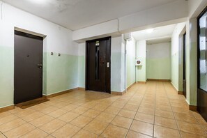 A hallway with tiled flooring, a black door, and a light switch on the wall. - City Apartment in Warsaw (Warszawa 2)
